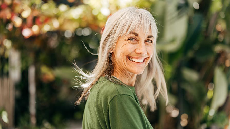 mulher a sorrir com o seu reflexo no espelho, simbolizando autoaceita&ccedil;&atilde;o e autoimagem positiva